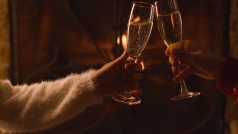 Close-Up-of-Two-People-Bringing-Their-Champagne-Glasses-Together-In-Front-of-Burning-Fireplace